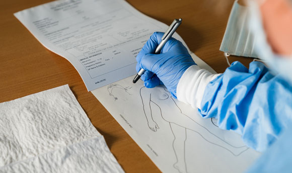 A person wearing scrubs demonstrates filling out a medical form.