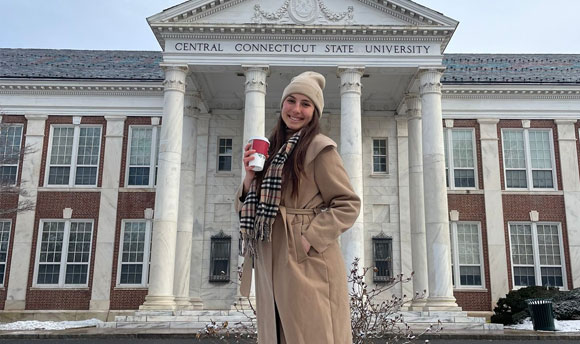 A young woman poses in front of the main Central Connecticut State University building