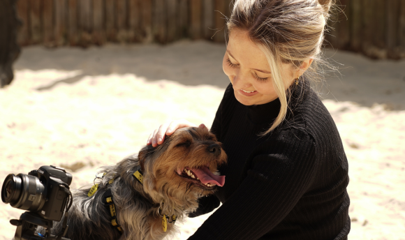 Graduate Leila Hay holding a camera and petting a dog.
