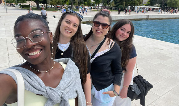 Four people pose for a group selfie together in front of a fountain.