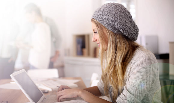 A young woman works on a laptop in a brightly lit room