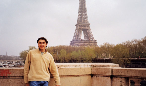 A young man stands in front of the Eiffel Tower