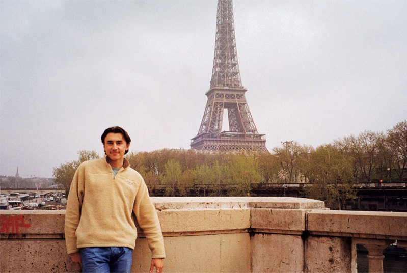 A young man stands in front of the Eiffel Tower