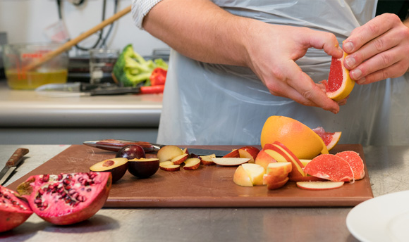 A person chopping various different fruits on a chopping board.
