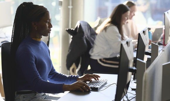 A female student sits at a computer in the library.