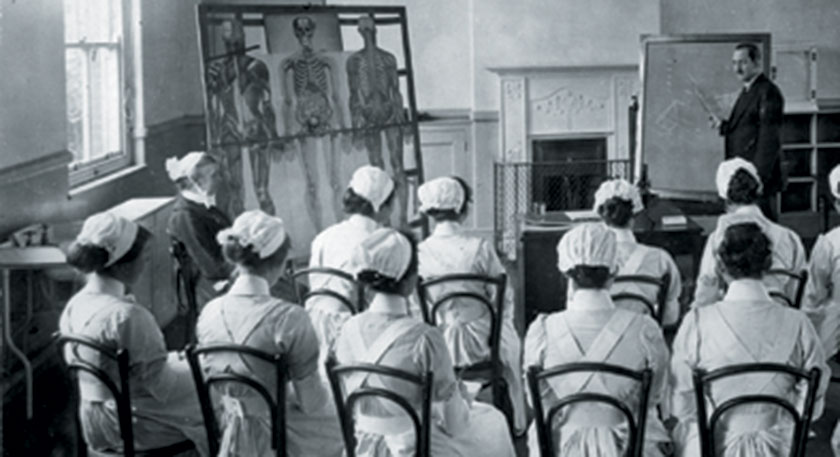 B+W photo of a nursing class being taught, there is a life size muscular-skeletal diagram