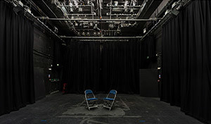 Empty performance room with two single folding chairs set up centre stage
