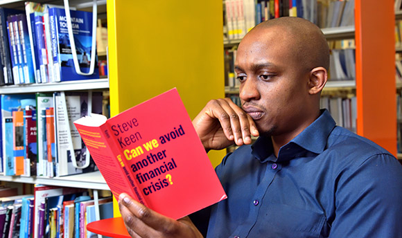 A young man sitting in the library, intently reading a book about financial crisis avoidance