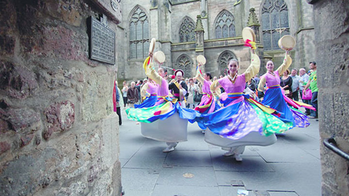 A group of dancers in brightly coloured dresses performing on the streets of Edinburgh