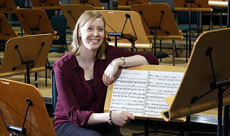 A young woman leaning on a sheet music stand and smiling at the camera 