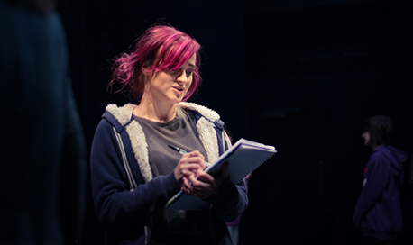 A QMU stage management student reading and making notes on a notepad on stage