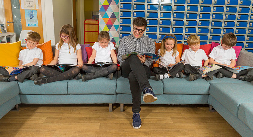 Teacher sitting on a sofa reading with some young students