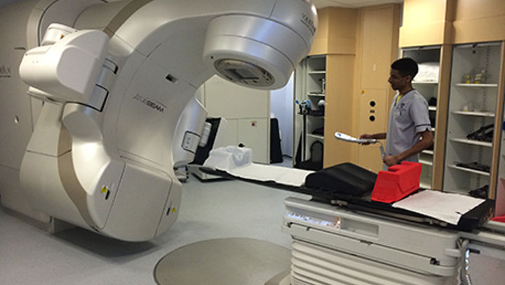 A QMU student standing beside a Radiotherapy machine