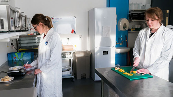 QMU Nutrition students writing down weight measurements and chopping ingredients in a kitchen