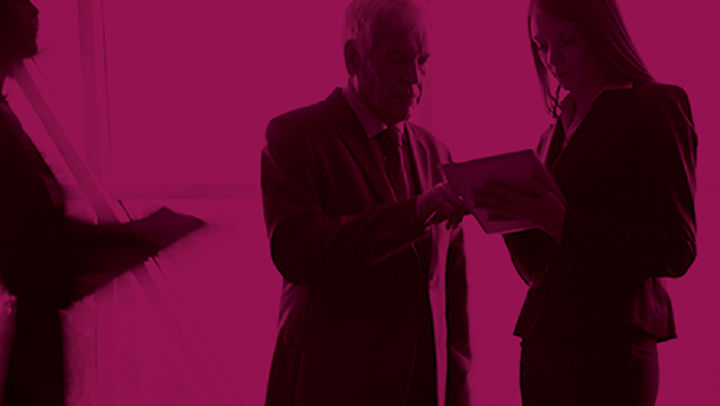 A black and pink photo of two professionals looking at paperwork as blurry people walk around them