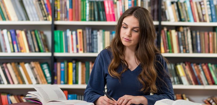 Student taking notes from books in library