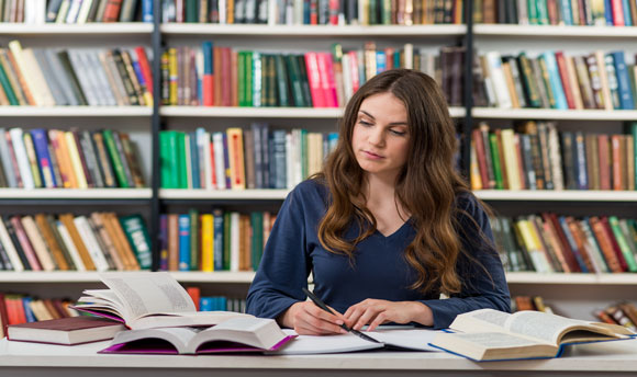 Student taking notes from books in library