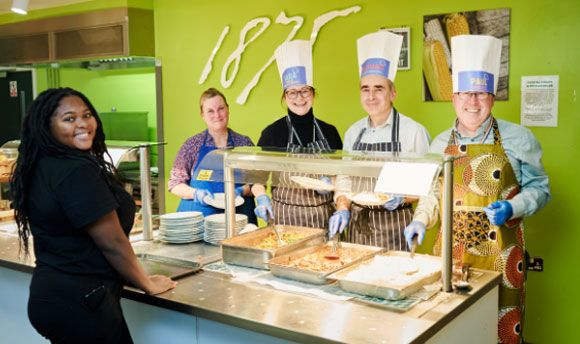 A young woman is served food from the QMU dining hall by several members of staff