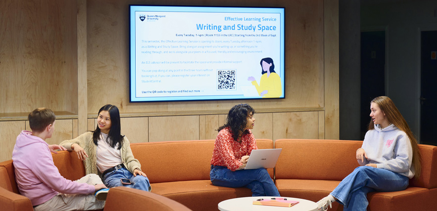 Four students sit on the curved, S-shaped sofa in the reception area of the library.
