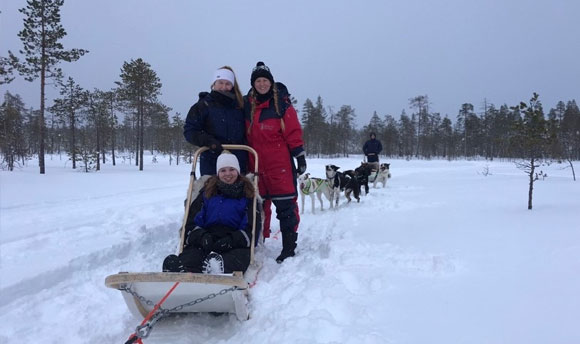 Three people ride on a sled drawn by huskies.