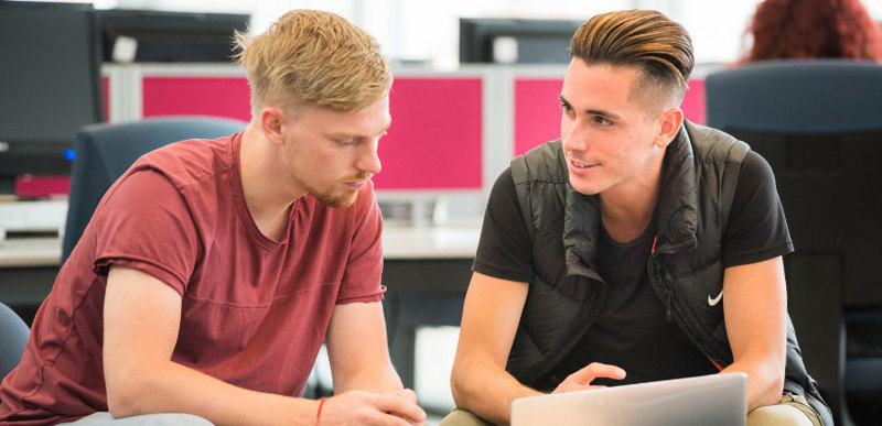 Two male students working together on a laptop device