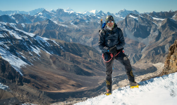 Mostafa Salameh stands on the top of a snowy mountain range in hiking gear.