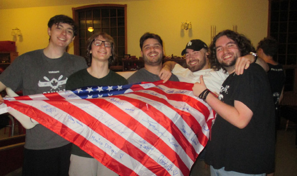 Four students holding another one up lengthways that is draped in a flag of the USA.