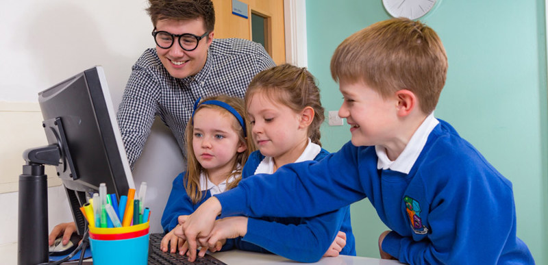 A young man showing a group of three primary school students how to use a computer