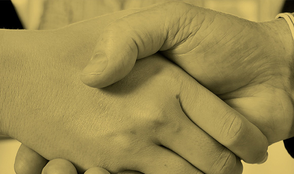 Close up photo of two people shaking hands, there is a yellow filter on the image.