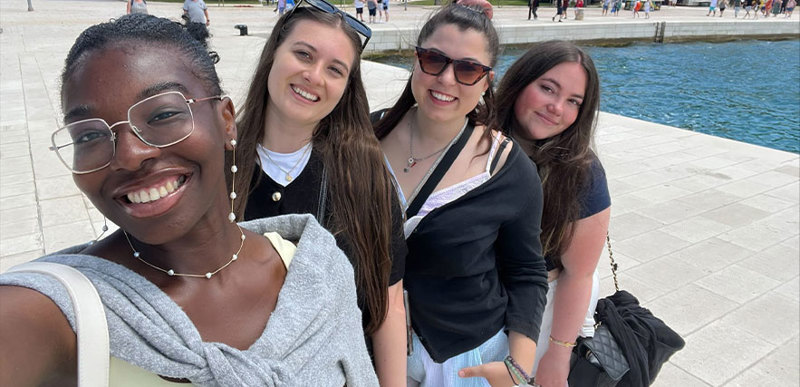 Four people pose for a group selfie together in front of a fountain.
