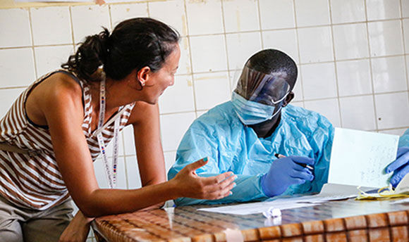 A woman leaning onto a table to talk to one of the nurses who is wearing full PPE