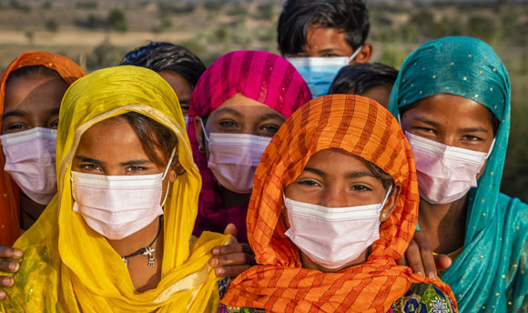 A large group of mostly young women wearing brightly coloured headscarves and white surgical masks.