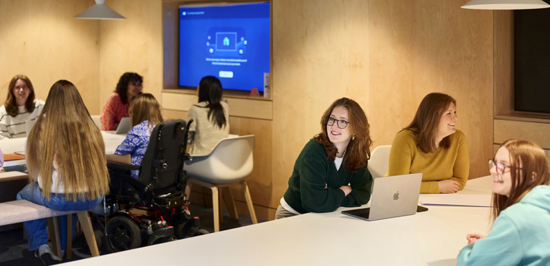 A group of students sit at the two long tables inside one of the library teaching spaces.