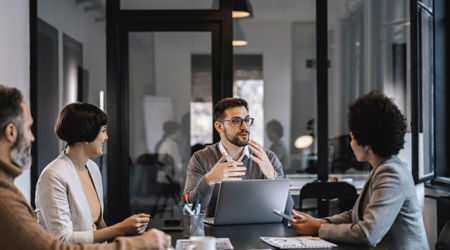 A group of working professionals sit at a meeting table having a lively discussion.