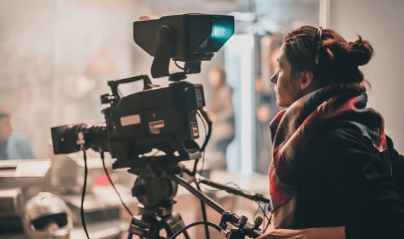 A young woman operates a large film camera.