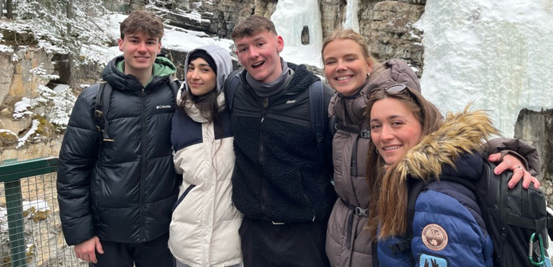 A group of people pose for a photo against a snowy mountain backdrop