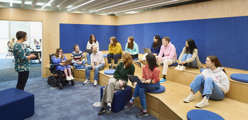 A lecturer speaks to a large group of students who are sitting on the tiered seating in one of the library's dedicated lecturing spaces.
