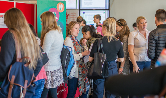 A group of people attending an event fair, in the background different stands and banners are visible.