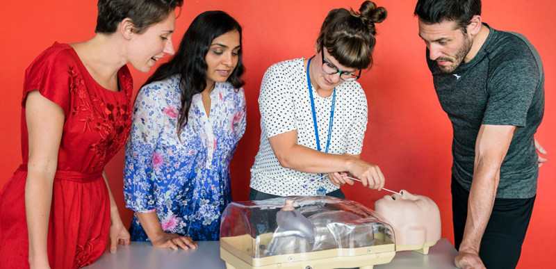 A group of people observing a demonstration of dietetics equipment on a see-through mannequin torso.