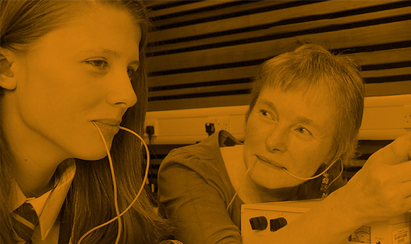 A young girl using the speech and language therapy equipment with a woman, there is an orange filter on the image.