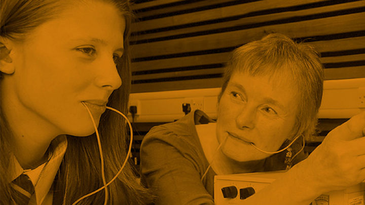 A young girl using the speech and language therapy equipment with a woman, there is an orange filter on the image.