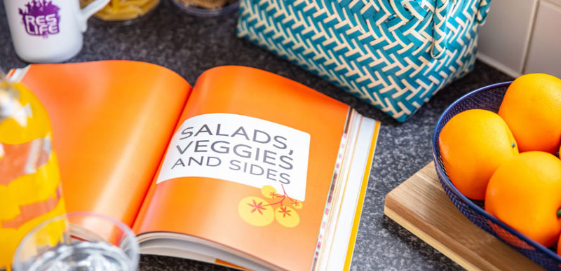A recipe book sits open on a kitchen counter. The text reads "Salads, veggies and sides".