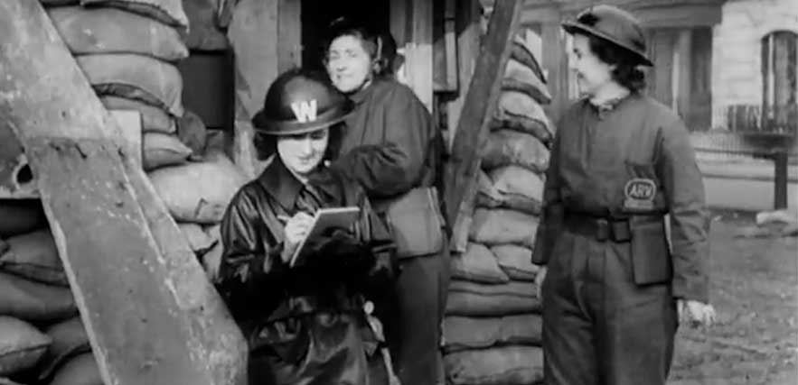 A black and white photograph of three women wearing military uniforms, surrounded by structures supported by sandbags.