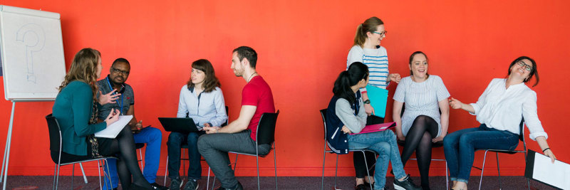 Two groups of students sitting on chairs and engaging in lively discussion together.