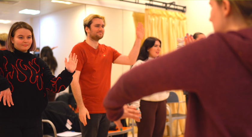 Students stand in a line and mimic dance moves to one another.