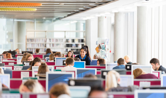 A view of the QMU library with students seated amongst various rows of computer desks.
