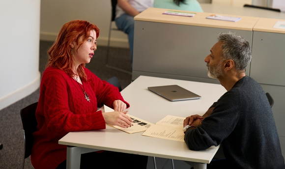 Female student sitting and speaking to male Student Services advisor