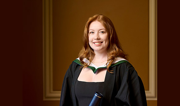 Portrait shot of student Tasmin McCallum with long red hair wearing graduation robe