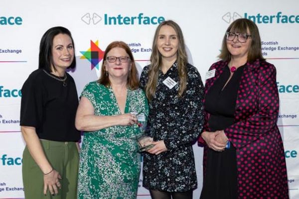 Four people pose for a photograph, holding an award won at the Interface Awards.