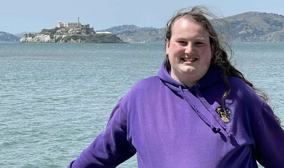 A young man stands on a boardwalk beside the ocean